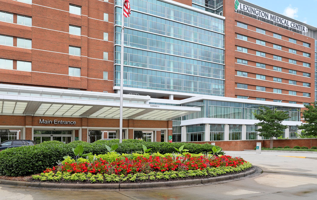 Hospital main entrance with a large flower bed and flagpole.