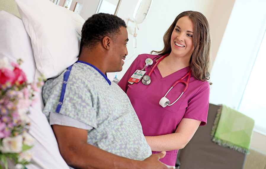 A nurse smiling at a patient resting in a hospital bed. 
