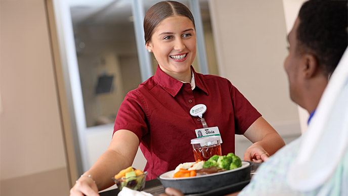 Nutrition Associate delivering a tray of food to a patient's room.