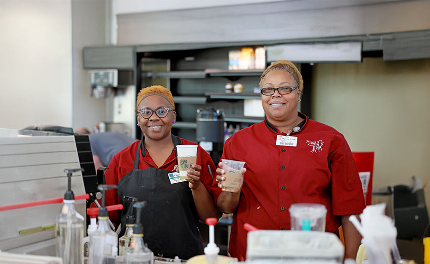 Two Starbucks workers smiling and holding Starbucks coffee.